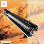 Tripode negro Moxom MX-SS20 con mecanismo de apertura automática y botón rojo en la base, sobre fondo de montaña.