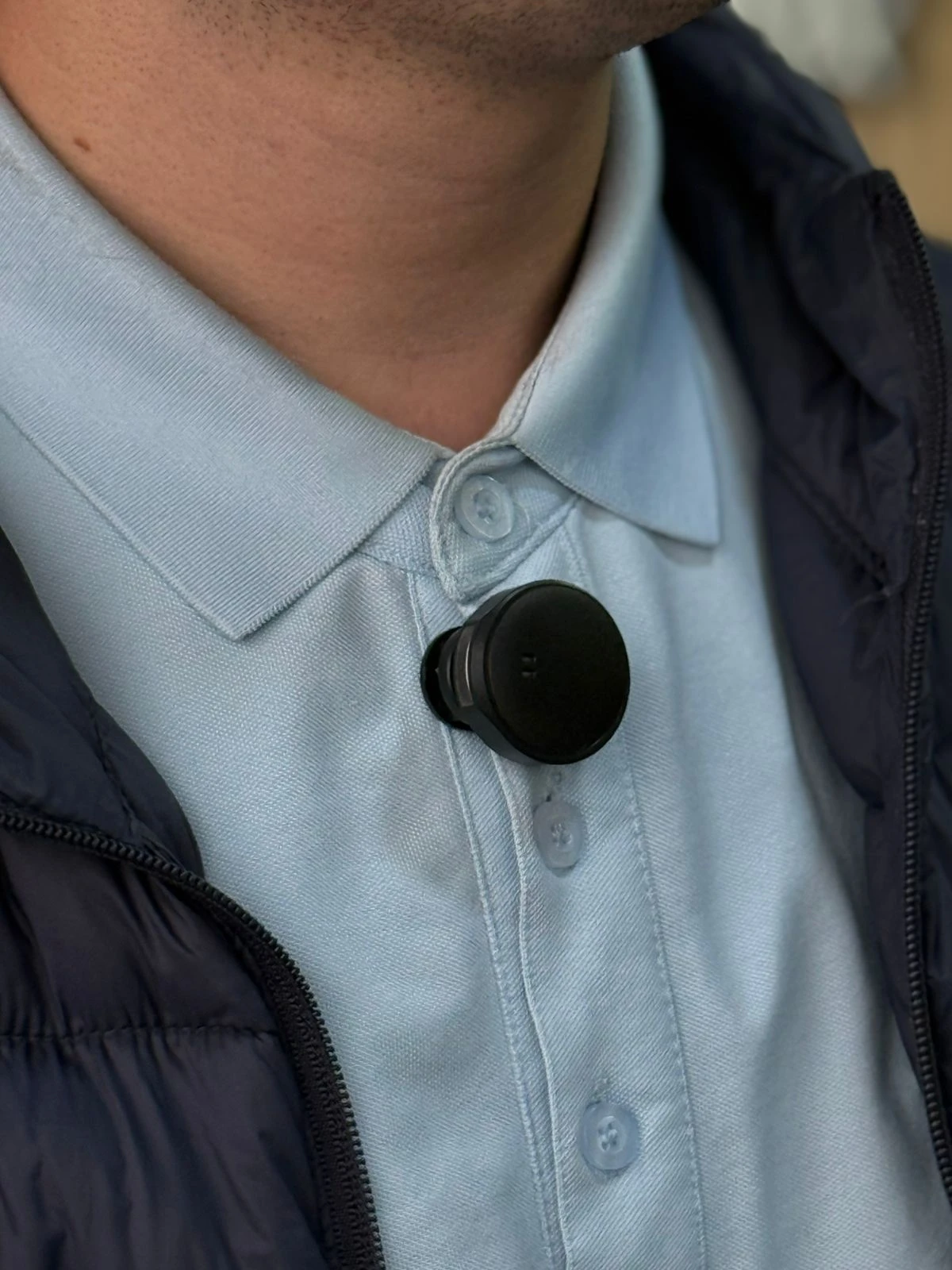 Micrófono solapa inalámbrico negro con batería integrada, colocado en la solapa de camisa azul claro, ideal para grabación profesional móvil.