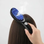 Cepillo masajeador capilar negro con cerdas azules y luz LED, en uso sobre cabello castaño.