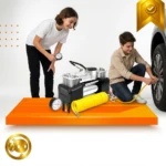 Compresor de aire portátil 12V con dos cilindros metálicos, manguera amarilla y manómetro, sobre plataforma naranja; dos personas inflan neumático de auto.