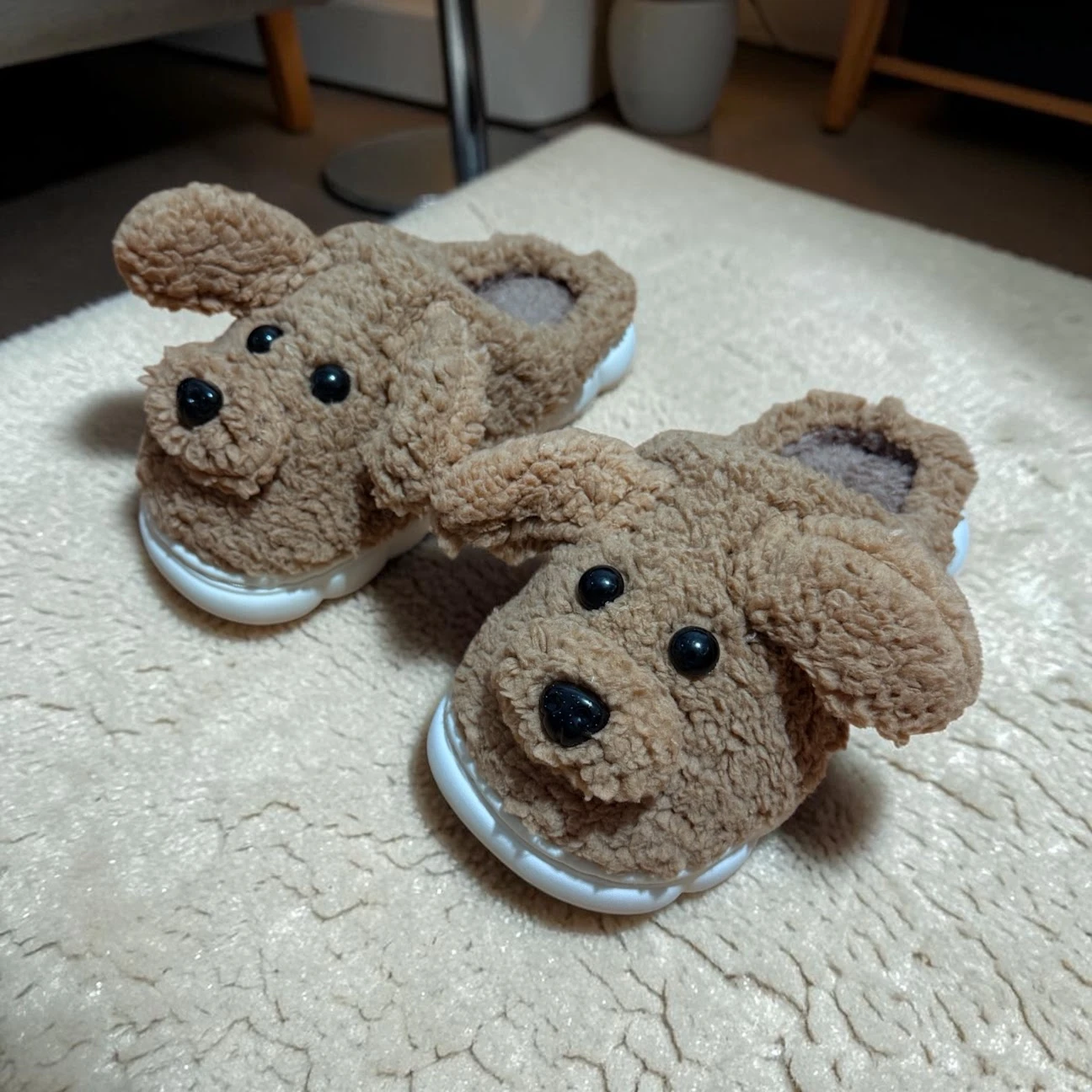 Pantuflas perrito café para niños, con suela blanca antideslizante y acolchado térmico, mostrando detalles de orejas y nariz negra sobre alfombra beige.