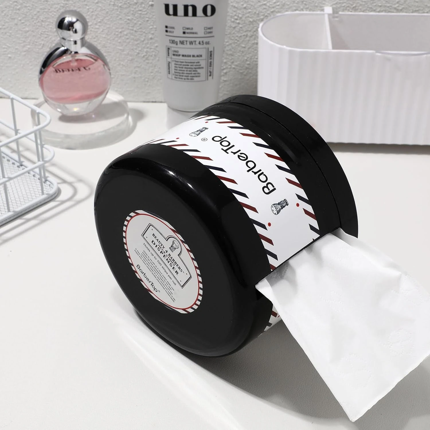 Dispensador de papel negro con salida lateral, diseño compacto sobre superficie blanca, con etiqueta visible y papel extendido.