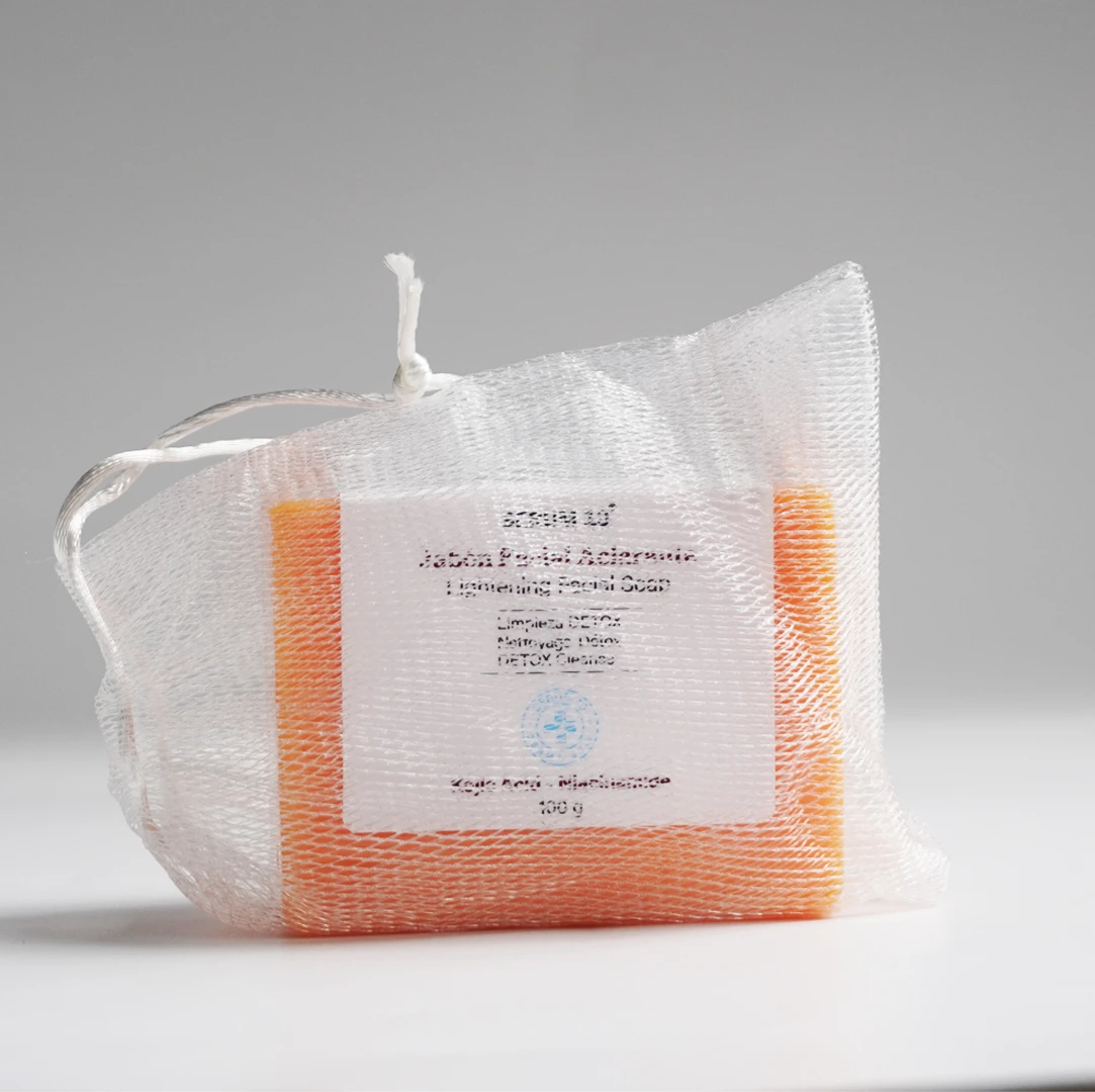 Jabón en barra naranja envuelto en malla blanca con etiqueta que indica Kojic y Niacinamida, presentación de 100 g.