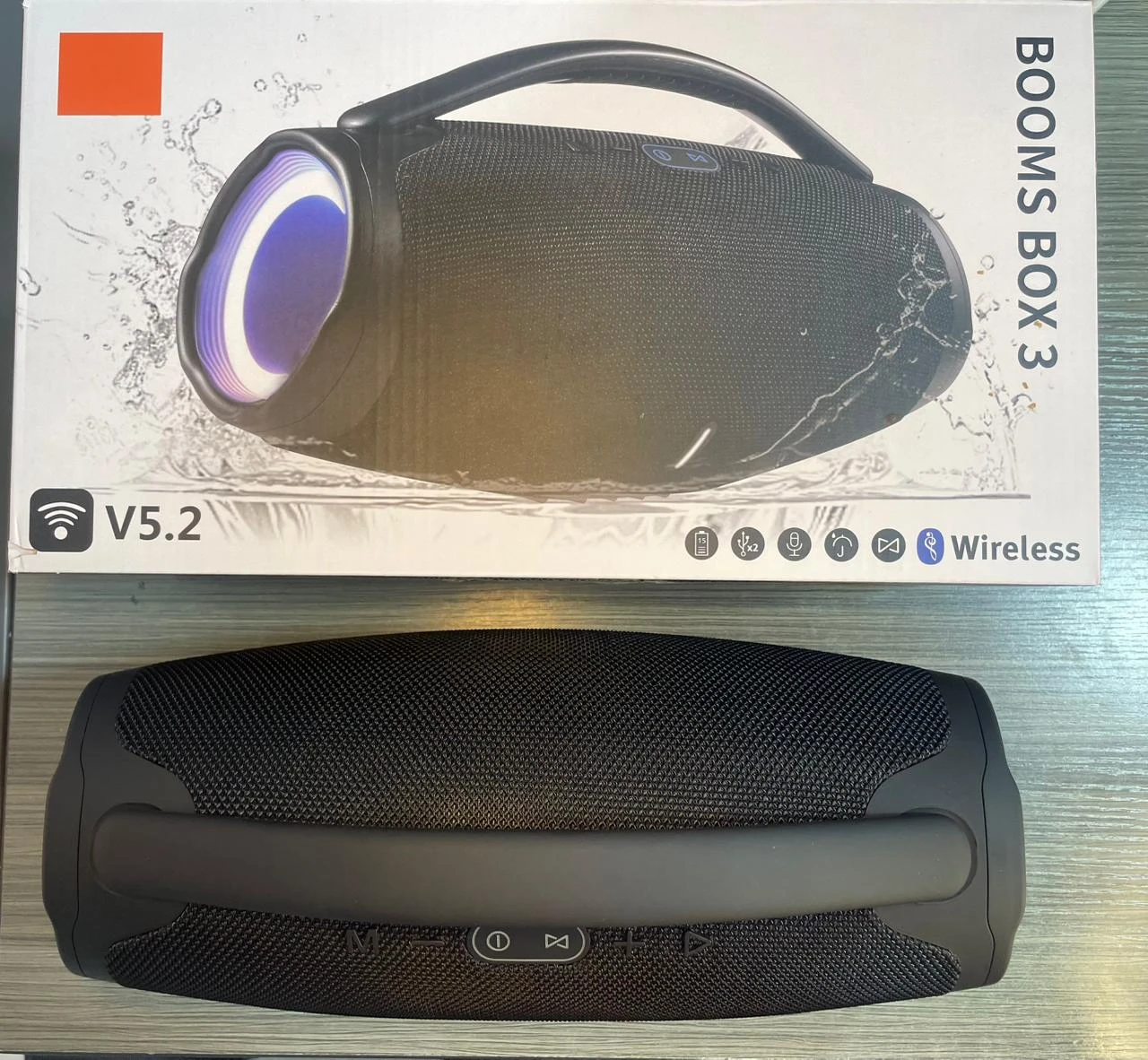 Parlante portátil negro con asa, caja de presentación y detalles en azul. Modelo Booms Box 3, resistente al agua, con luces LED y conectividad Bluetooth.