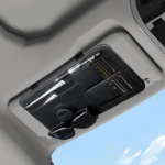 Organizador negro para visera de carro, con compartimentos para documentos, dinero y gafas de sol, instalado en techo de vehículo.