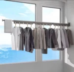 Tendedero extensible plegable contra pared en color gris oscuro, con ropa colgada y ventana al fondo.