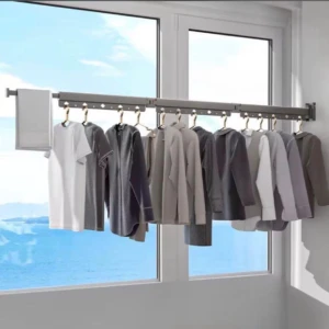 Tendedero extensible plegable contra pared en color gris oscuro, con ropa colgada y ventana al fondo.