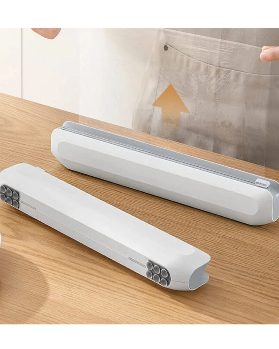 Dispensador magnético blanco con cortador invisible sobre mesa de madera, mostrando dos unidades en ángulo lateral.