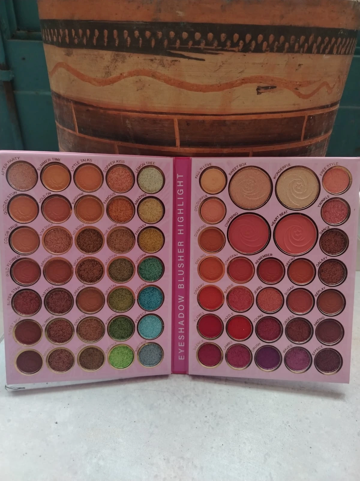 Paleta profesional de 65 sombras y brillos en tonos cálidos, fríos y neutros, abierta mostrando disposición de colores y texturas.
