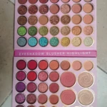 Paleta profesional de 65 sombras con tonos mate y shimmer, organizadas en tres secciones: ojos, mejillas y brillos, sobre fondo rosa claro.