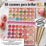 Paleta de maquillaje profesional con 65 tonos de sombras, blushers y highlighters en presentación rosa, rodeada de rosas y brochas doradas.