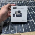 Caja blanca del micrófono inalámbrico SX23, mostrando su diseño compacto con receptor y micrófono de solapa, sobre fondo de múltiples unidades envasadas.