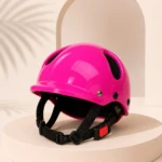 Casco rosa brillante con ventilación lateral, correa negra y hebilla roja, sobre pedestal blanco con fondo minimalista.
