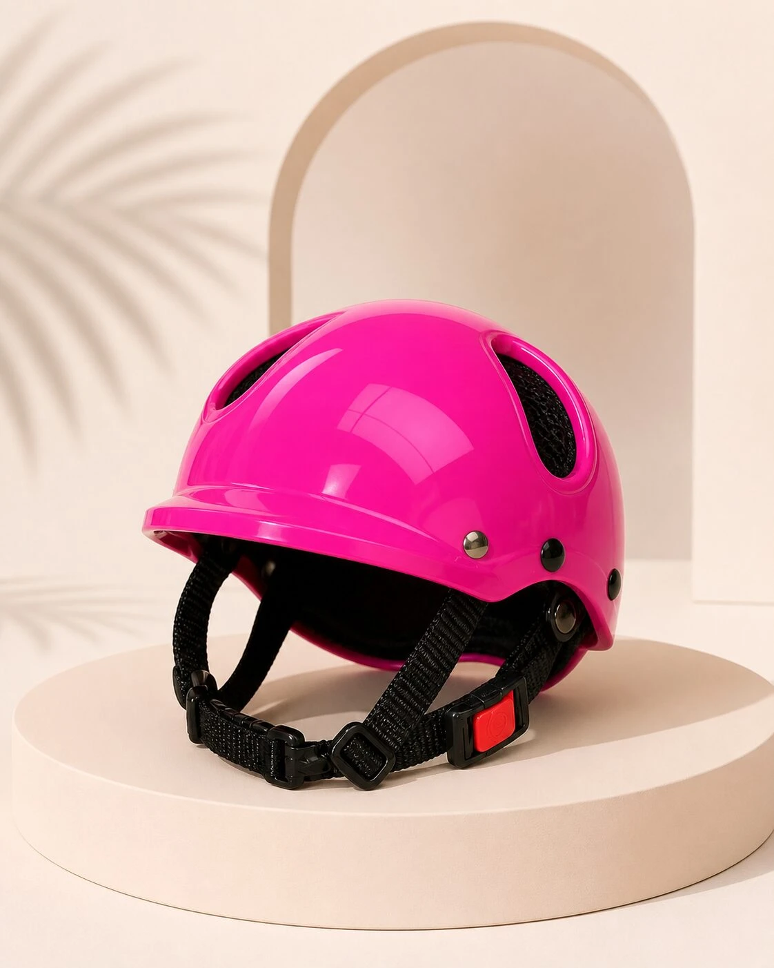 Casco rosa brillante con ventilación lateral, correa negra y hebilla roja, sobre pedestal blanco con fondo minimalista.