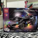 Coche deportivo a control remoto en caja, modelo negro con luces LED multicolor y detalles reflectantes, sobre tela estampada zebra.