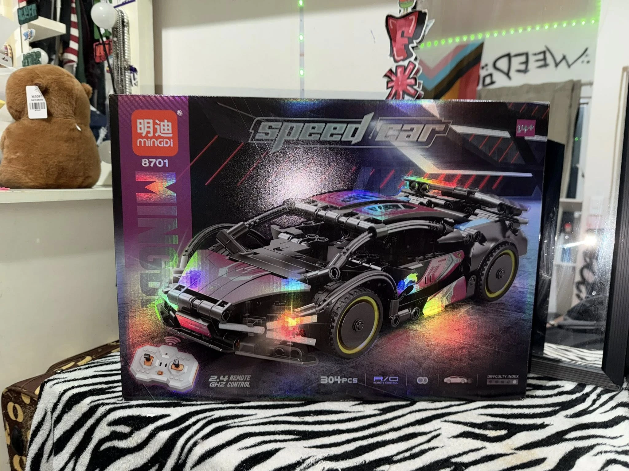 Coche deportivo a control remoto en caja, modelo negro con luces LED multicolor y detalles reflectantes, sobre tela estampada zebra.