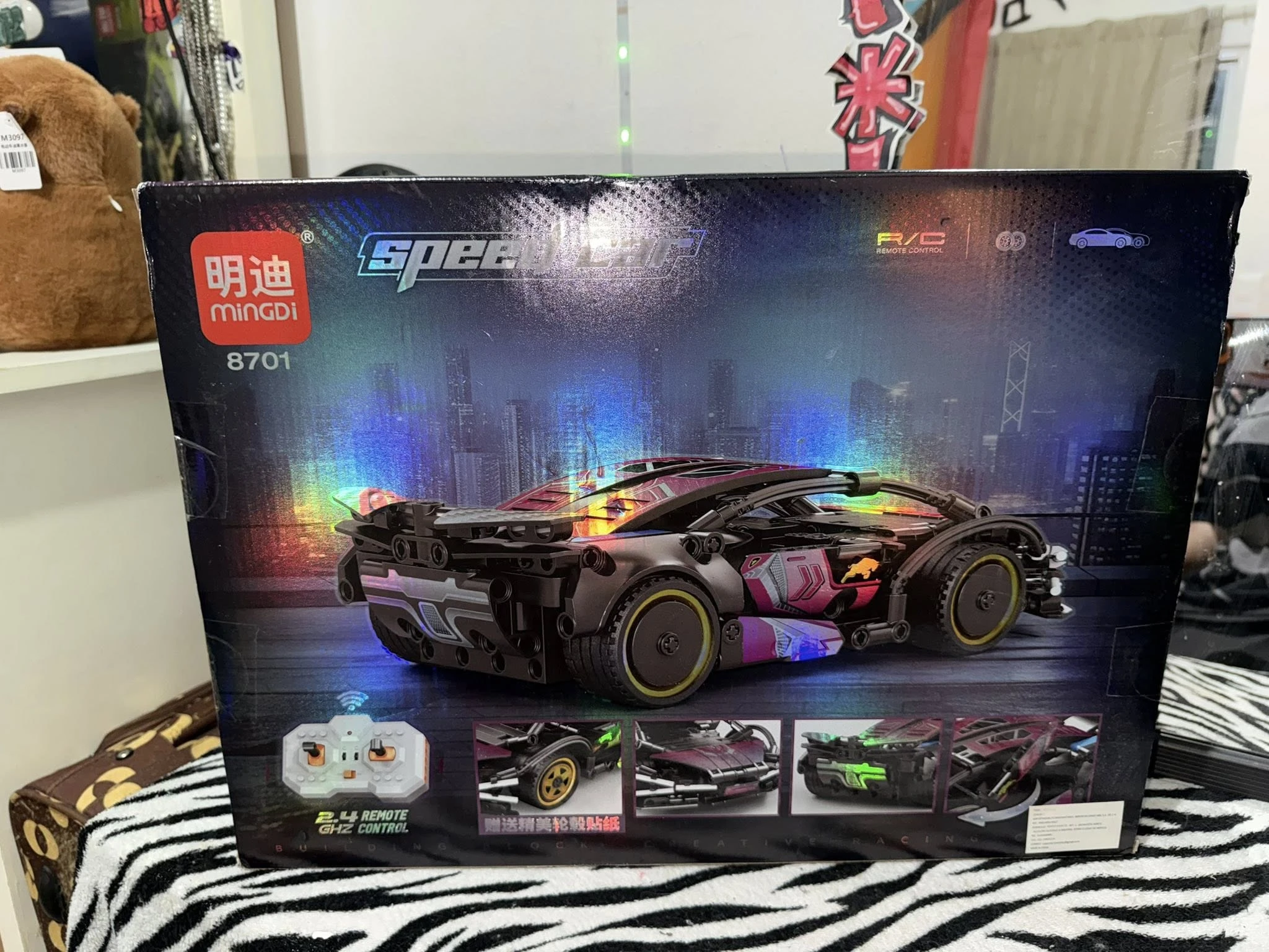 Caja del set de construcción Mingdi 8701, mostrando un coche deportivo negro con detalles multicolores y luces LED, sobre fondo urbano nocturno. Incluye mando a distancia y accesorios visibles en la parte inferior.
