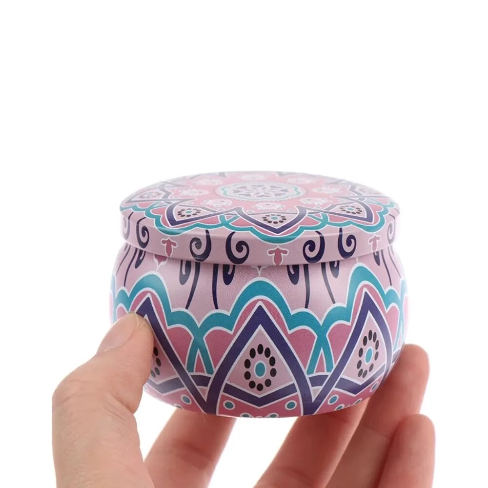 Vela aromática de soya en tarro redondo con tapa, diseño geométrico en tonos rosa, azul y morado, sostenida en mano.