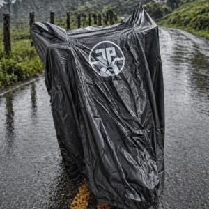 Cubierta impermeable negra para motocicleta, con logo circular blanco en la parte frontal, colocada sobre una moto estacionada en carretera mojada bajo lluvia.