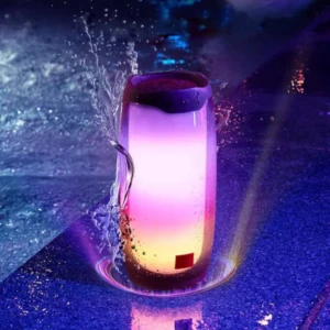 Parlante Remax resistente al agua con luces LED en tonos púrpura y rosa, mostrando gotas de agua salpicando su superficie durante uso bajo lluvia.