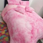 Edredón térmico peludo rosa con diseño degradado, colocado sobre cama doble con cabecero azul oscuro y cojines a juego.