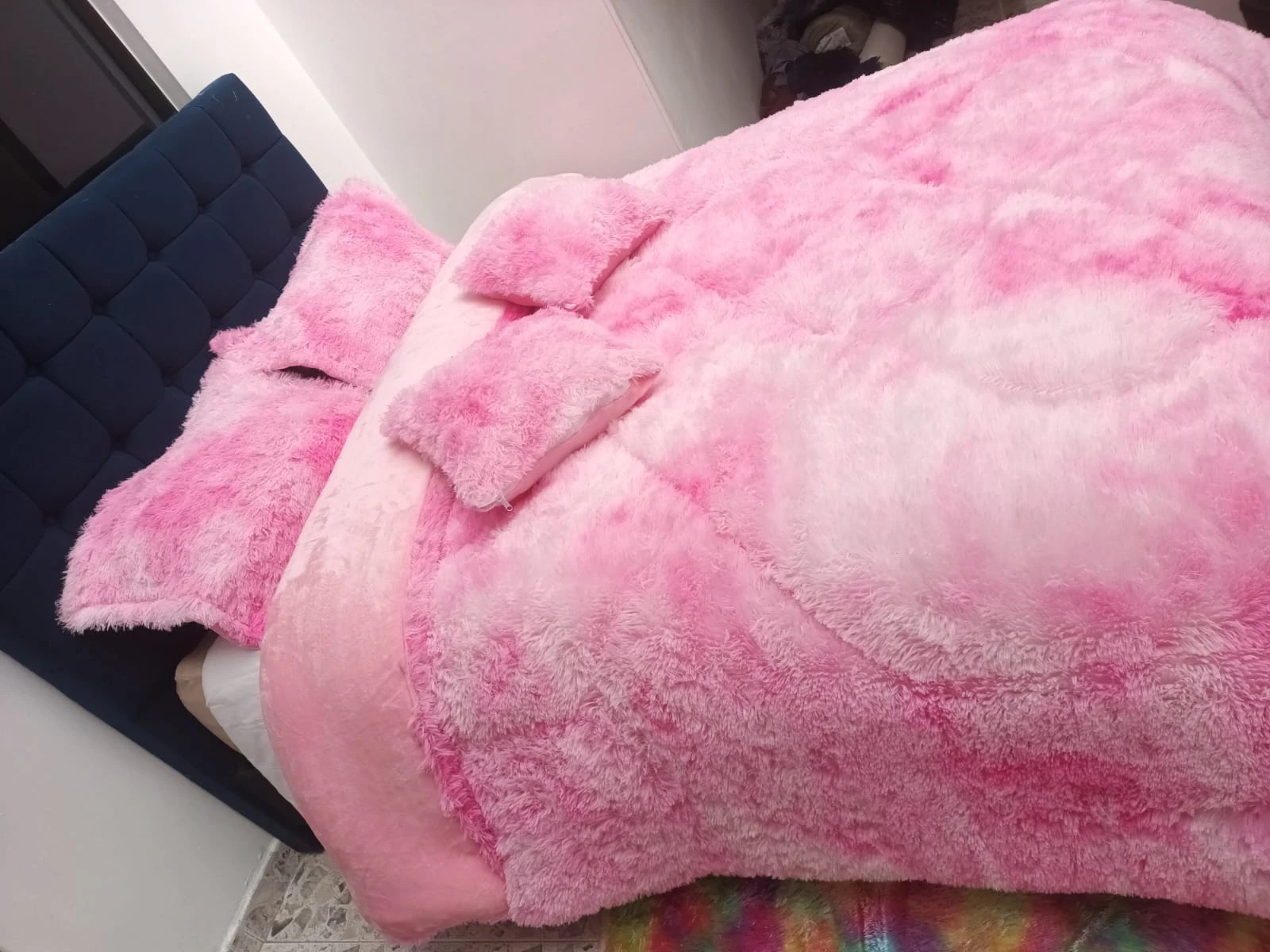 Edredón térmico peludo rosa sobre cama con cabecero azul, textura suave y voluminosa, ideal para invierno.