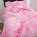 Edredón térmico peludo rosa con estampado degradado, sobre cama doble con cabecero tapizado en azul oscuro.