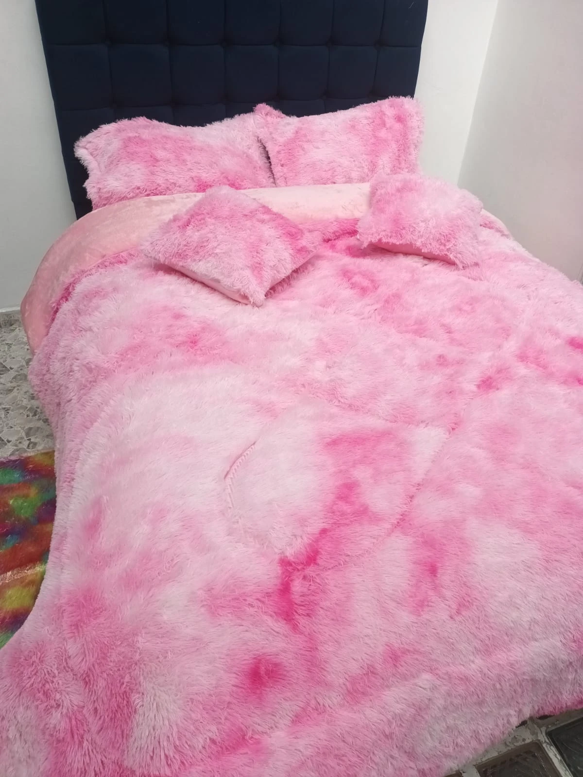 Edredón térmico peludo rosa con estampado degradado, sobre cama doble con cabecero tapizado en azul oscuro.