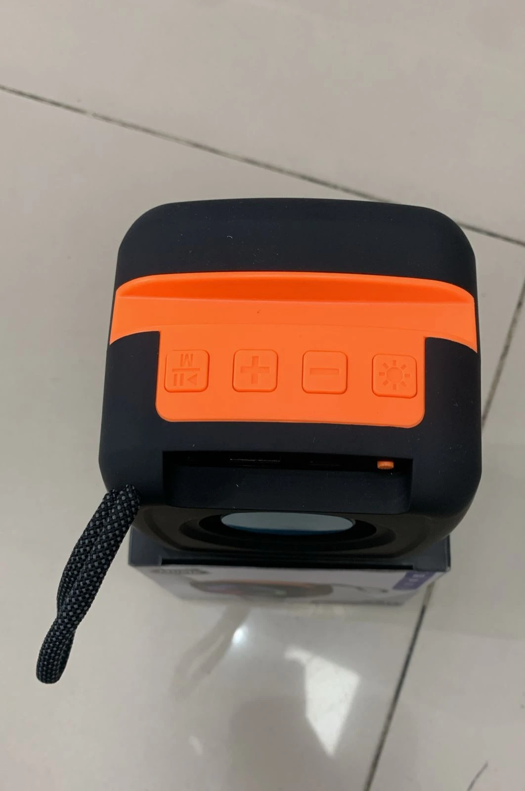 Parlante Bluetooth negro con detalles naranjas, visto desde arriba, mostrando controles táctiles y asa de transporte.
