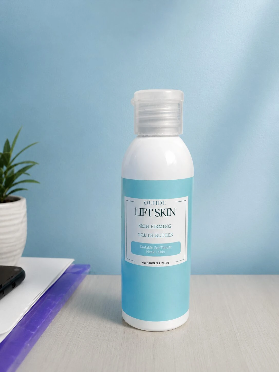 Botella de crema reafirmante Lift Skin en tono azul claro, con etiqueta blanca y tapa transparente, sobre superficie clara junto a cuaderno y planta.