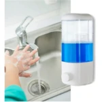 Dispensador de jabón líquido transparente con cuerpo blanco y líquido azul, montado en pared junto a fregadero; manos lavándose bajo grifo.