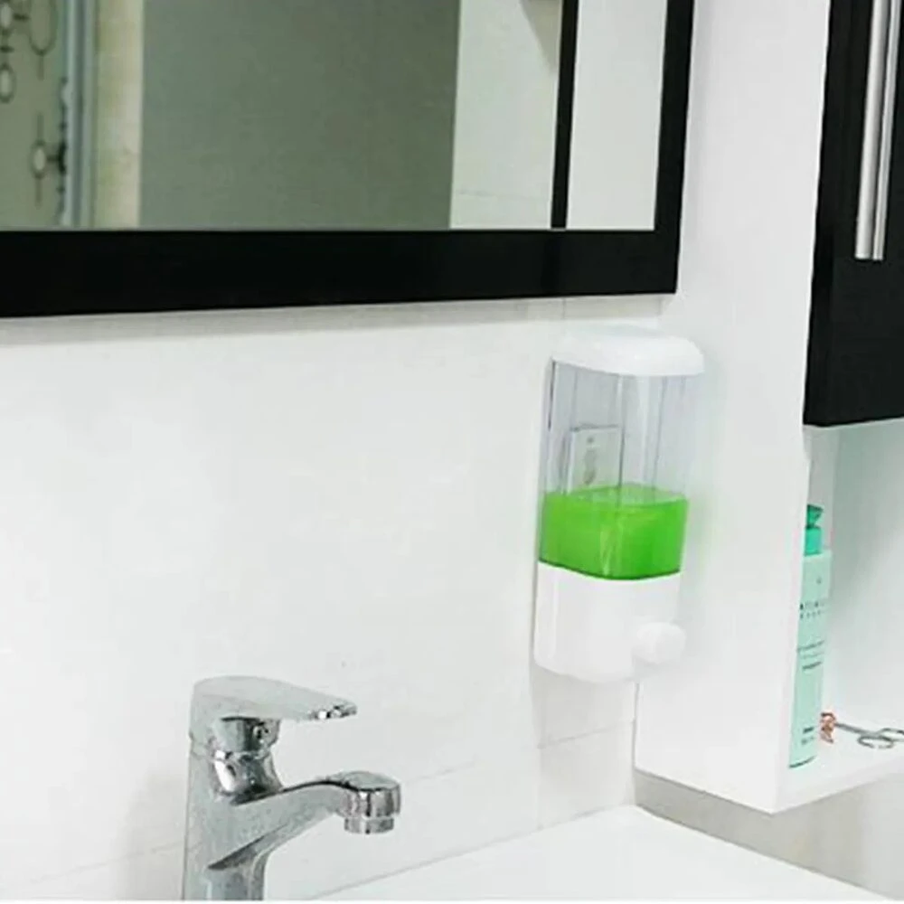 Dispensador de jabón líquido transparente de 500 ml en ABS, con líquido verde, montado en pared junto a lavabo y espejo.