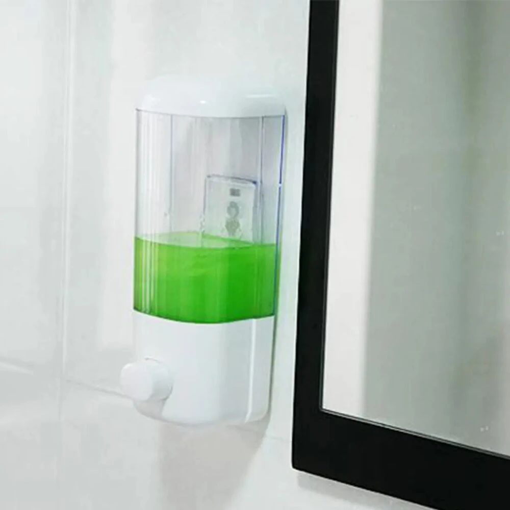 Dispensador de jabón líquido transparente de 500 ml en ABS, con líquido verde visible y dispensador blanco montado en pared junto a espejo.