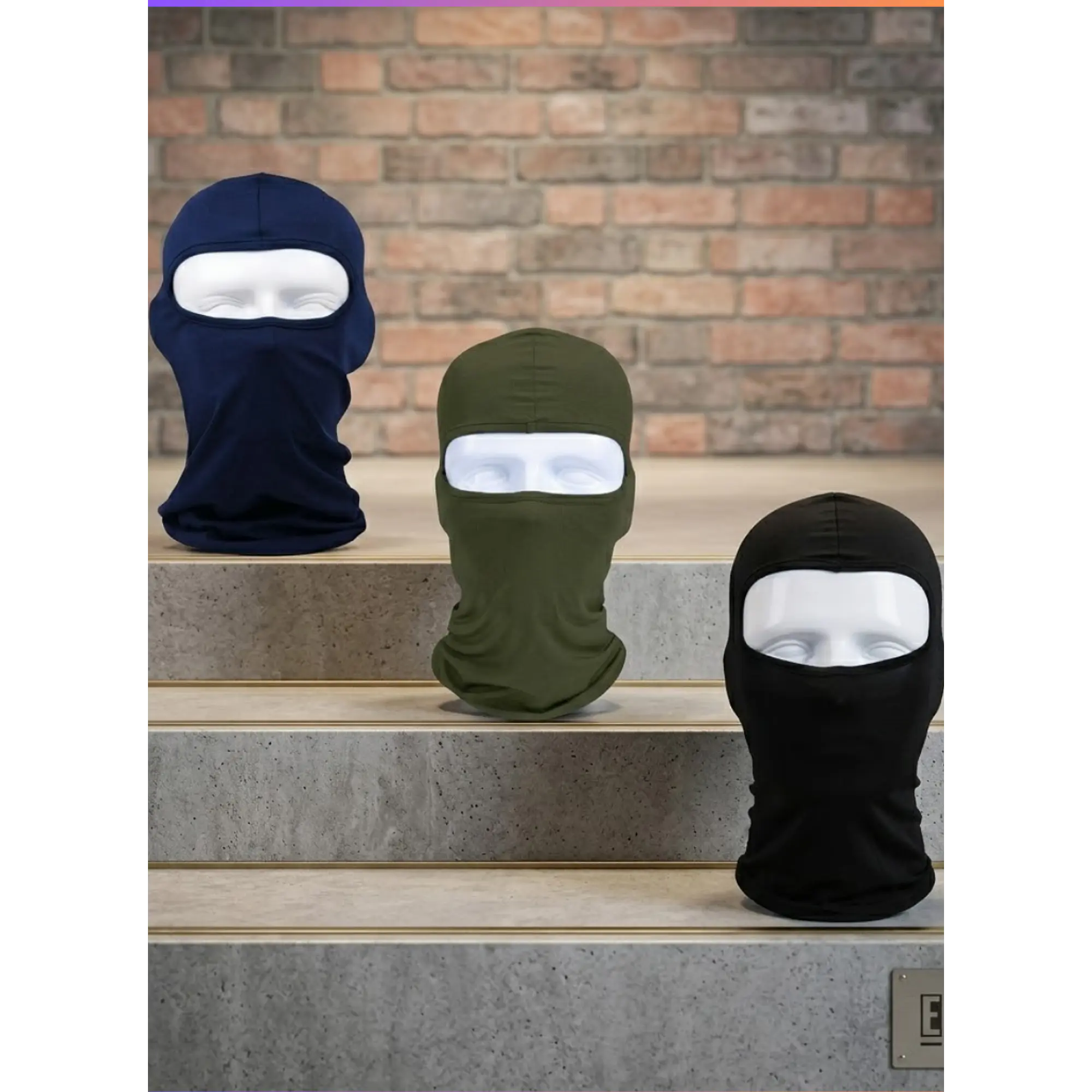 Tres balaclavas de algodón liso en azul marino, verde oliva y negro, exhibidas sobre escalones de concreto con fondo de ladrillo.