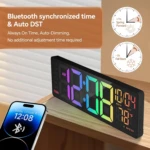 Reloj despertador digital negro con dígitos LED RGB multicolor, fecha y temperatura, sincronizado por Bluetooth con un celular sobre madera.