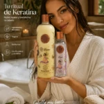 Mujer con bata blanca sosteniendo botella grande de champú Keratina y frasco pequeño de tratamiento, ambos con etiquetas ilustradas y tapas doradas, en baño con toallas y velas.