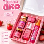 Caja rosa abierta mostrando cinco productos de cuidado personal: dos frascos con tapa dorada, un tubo, un spray y un envase cilíndrico, sobre fondo con fresas y texto en español.