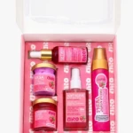 Kit de viaje en caja rosa con cinco productos: dos frascos de crema, un frasco de jabón íntimo, un spray y un tubo de colágeno. Todos con etiquetas en tonos rosas y dorados.