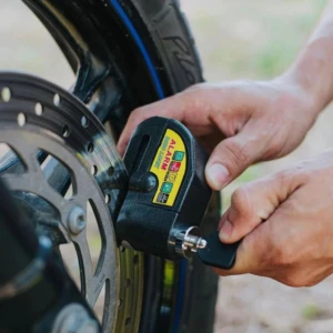Candado de disco negro para moto con alarma, siendo instalado en el disco de freno de una rueda trasera.