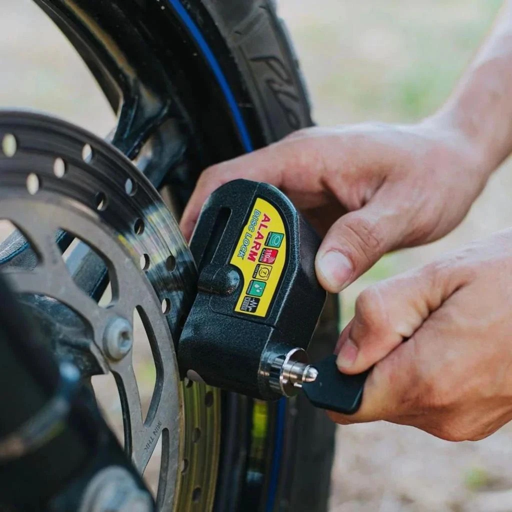 Candado de disco negro para moto con alarma, siendo instalado en el disco de freno de una rueda trasera.