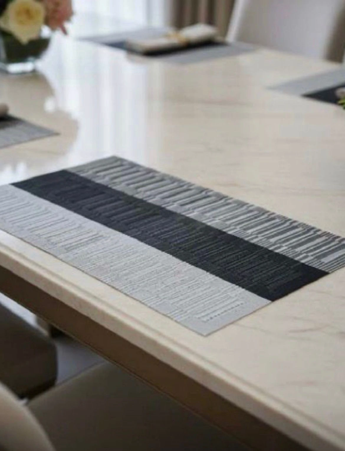 Mantel rectangular bicolor gris con textura nórdica, colocado sobre mesa de comedor de superficie clara.