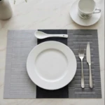 Mantel rectangular bicolor gris y negro con textura nórdica, colocado sobre mesa blanca con vajilla y cubiertos.