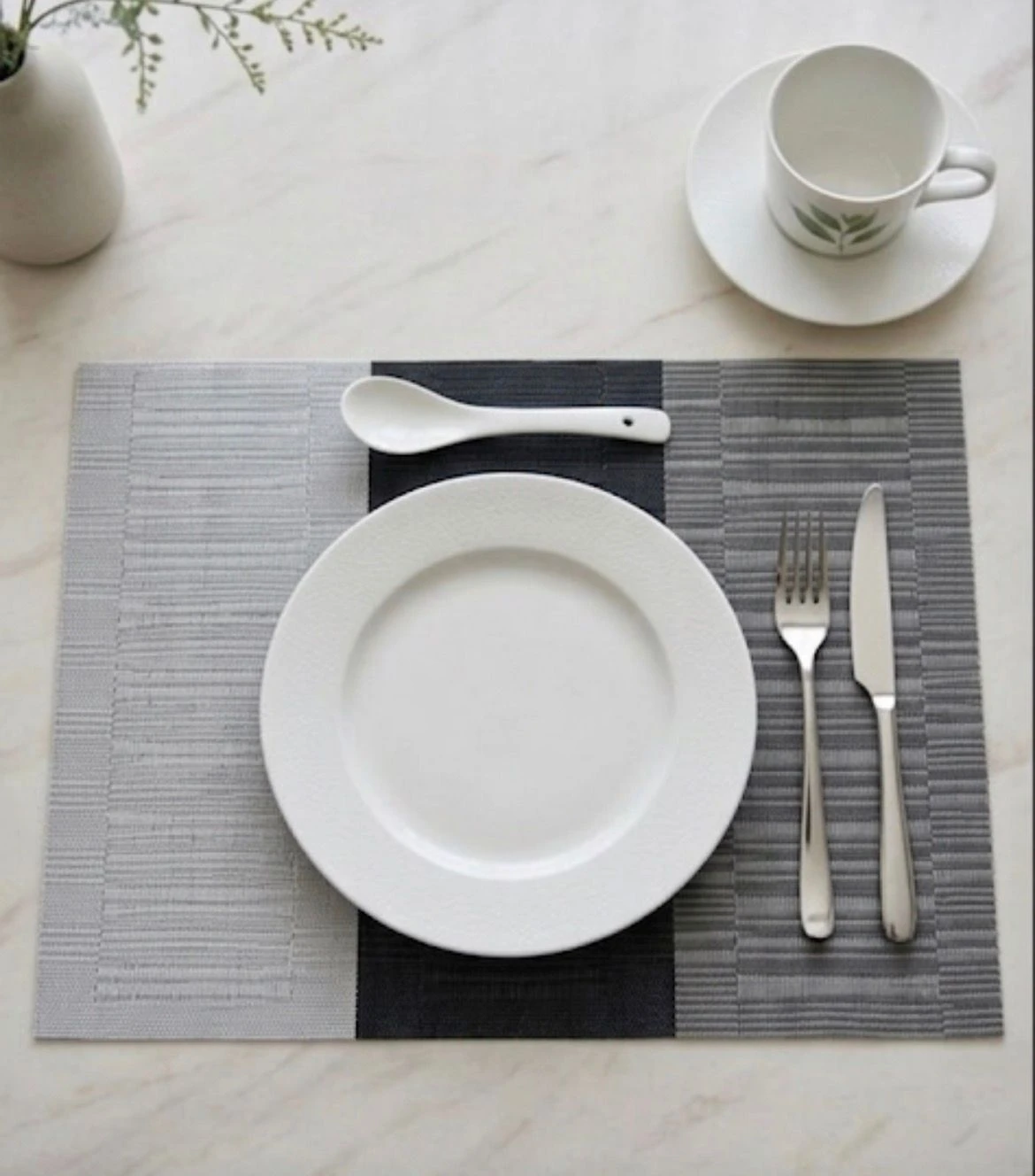 Mantel rectangular bicolor gris y negro con textura nórdica, colocado sobre mesa blanca con vajilla y cubiertos.