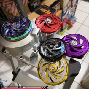 Cinco tapas giratorias de aluminio anodizado en colores rojo, azul, negro, morado y dorado, montadas sobre un soporte metálico en entorno de almacén.