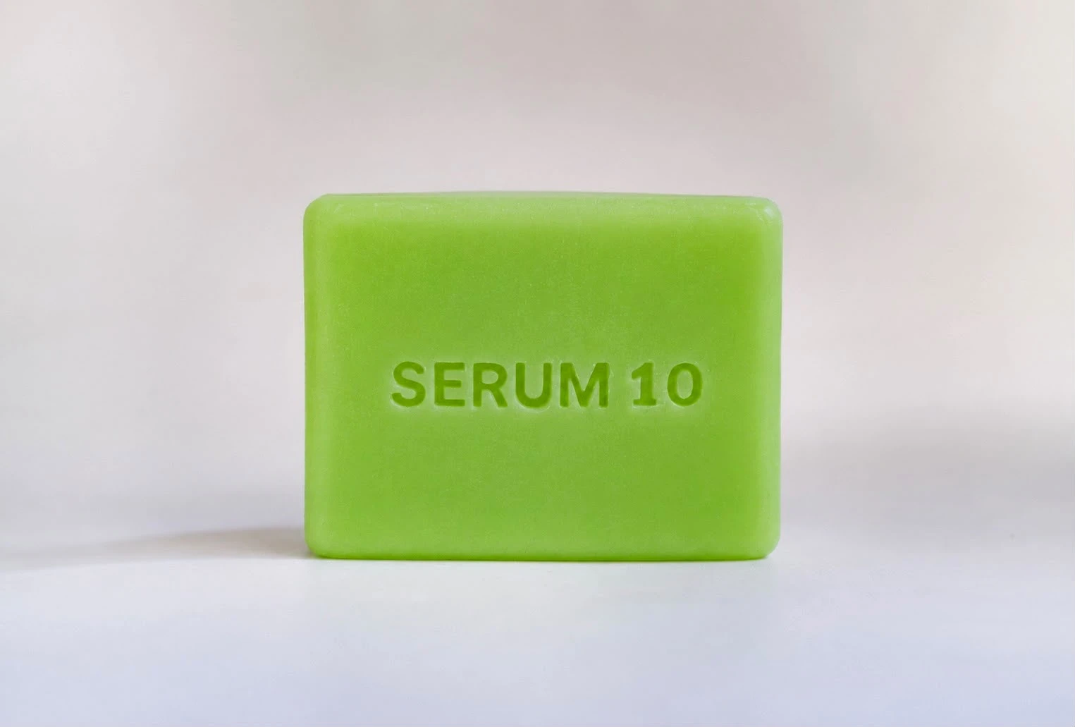 Jabón facial verde con la inscripción SERUM 10 en relieve, sobre fondo blanco. Presentación individual del producto.