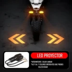 Proyector LED direccional con luz amarilla intermitente y flechas proyectadas en el suelo, mostrando cableado y conectores incluidos.