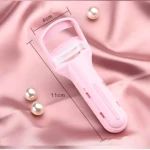 Rizador de pestañas manual ergonómico en color rosa pastel, con medidas de 11 cm de largo y 4 cm de ancho, sobre tela rosa con perlas decorativas.