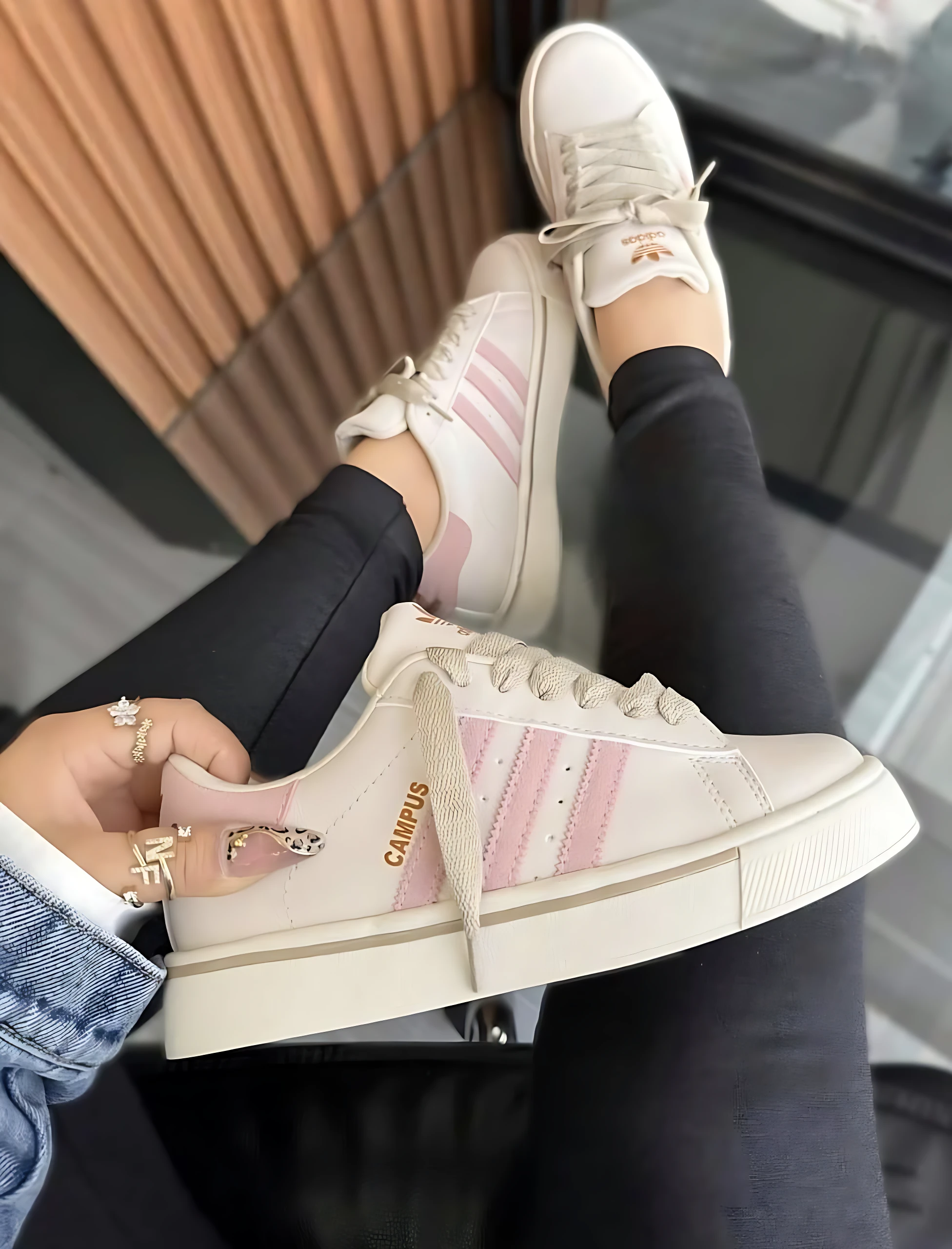Zapatilla Adidas Campus dama en color crema con detalles rosa, suela acolchada y logo visible, vista de perfil sobre fondo urbano.