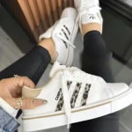 Zapatilla Adidas Campus blanca con detalles en estampado animal y suela acolchada, vista lateral y superior, usada por mujer con pantalón negro.