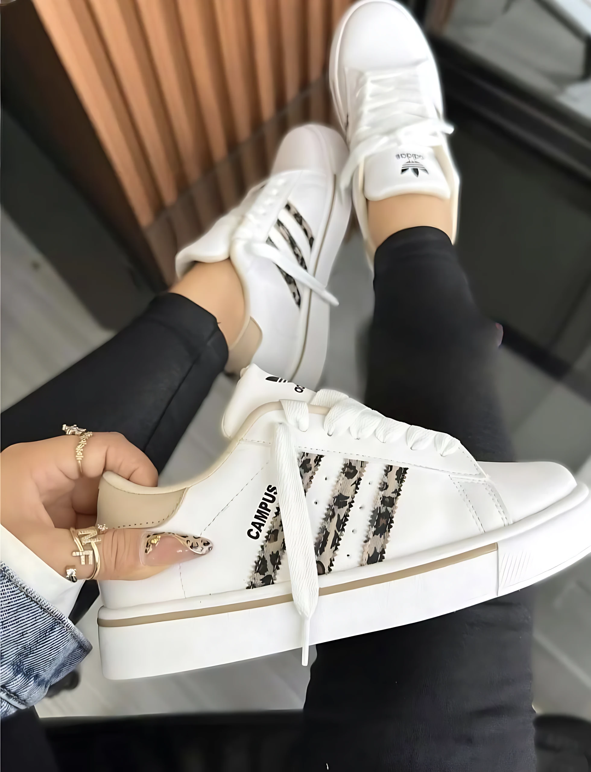 Zapatilla Adidas Campus blanca con detalles en estampado animal y suela acolchada, vista lateral y superior, usada por mujer con pantalón negro.